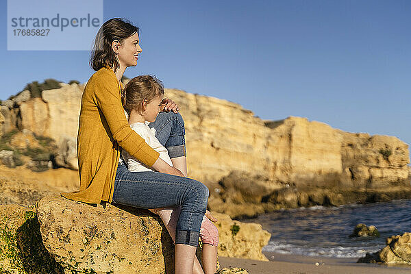 Glückliche Frau und Tochter sitzen auf einem Felsen am Strand