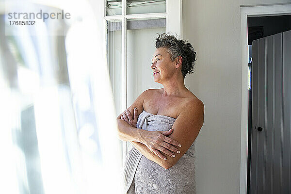 Smiling woman wearing towel standing with arms crossed at home