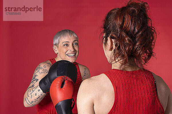 Glückliche Frau boxt mit Freund vor rotem Hintergrund