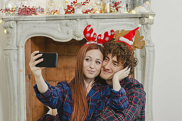 Smiling couple wearing Christmas headdress taking selfie through smart phone