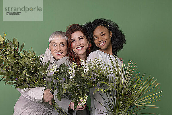 Fröhliche gemischtrassige Freunde mit Pflanzen vor grünem Hintergrund