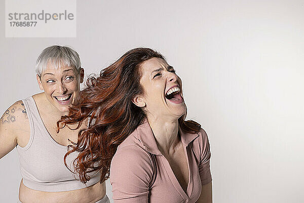 Lachende rothaarige Frau  die Spaß mit ihrer Freundin vor weißem Hintergrund hat
