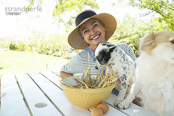 Lächelnde Frau und Hunde sitzen mit Eierschüssel am Tisch im Garten