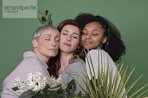 Multiracial friends with eyes closed standing against green background