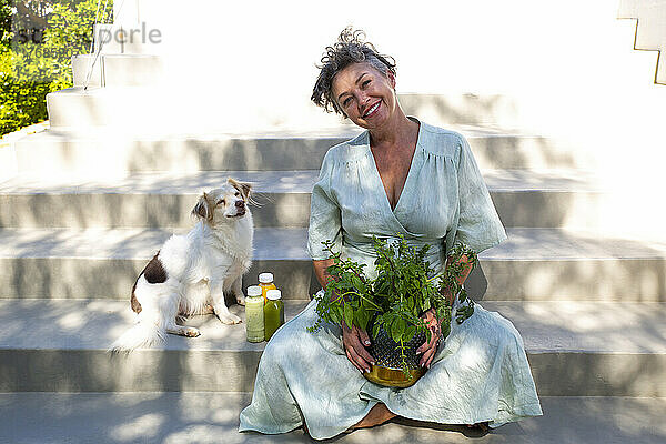 Glückliche Frau mit Pflanze sitzt neben Hund auf Stufen