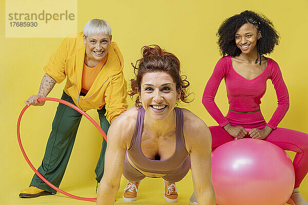 Fröhliche  gemischtrassige Freunde mit Fitnessgeräten vor gelbem Hintergrund