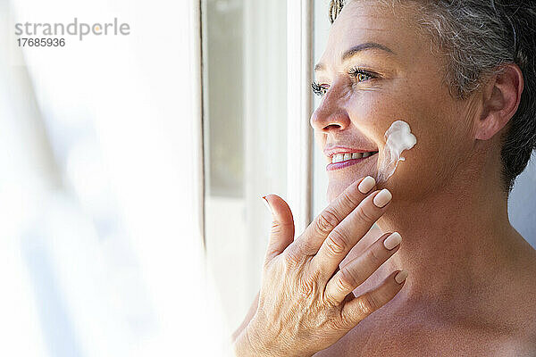Lächelnde reife Frau  die Feuchtigkeitscreme auf ihr Gesicht aufträgt