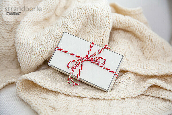 Geschenkbox mit rot-weißer Schnur auf Wolldecke gewickelt