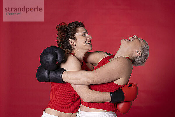 Fröhliche Freunde mit Boxhandschuhen  die sich vor rotem Hintergrund umarmen