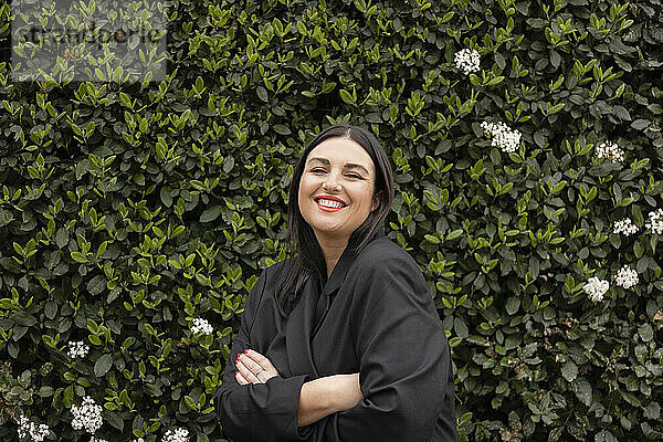 Happy woman wearing black blazer standing in front of green plant wall