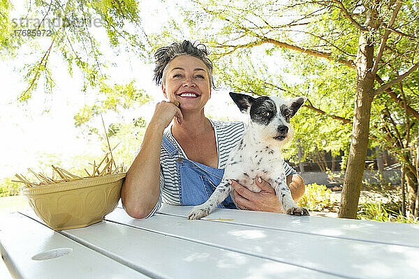 Frau sitzt mit Hund am Tisch im Garten