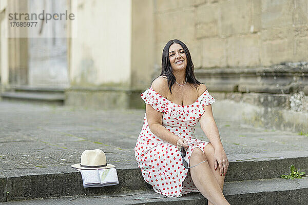 Lächelnde Frau im gepunkteten Kleid sitzt auf Stufen