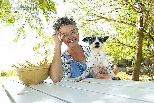Lächelnde Frau mit Hund am Tisch im Garten