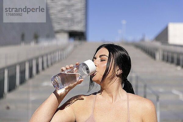 Frau trinkt Wasser aus einer Flasche vor der Treppe