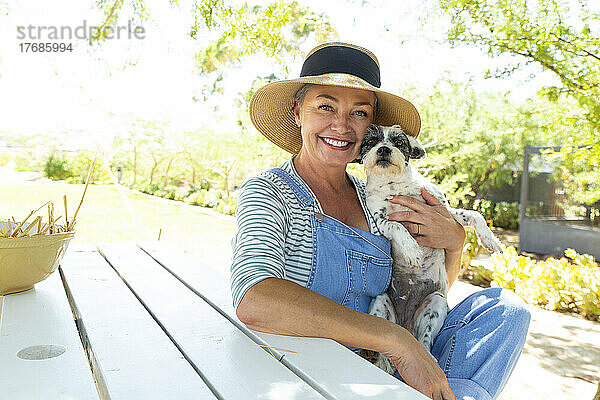 Lächelnde Frau mit Hund sitzt am Tisch im Garten