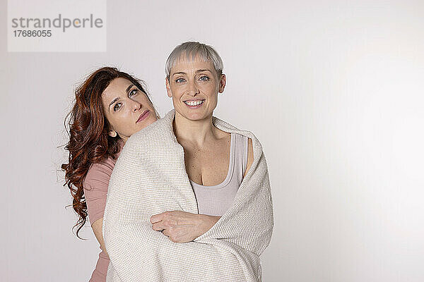 Smiling woman wrapped in blanket standing with friend against white background