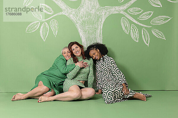 Glückliche Freunde sitzen auf dem Boden vor einer grünen Wand