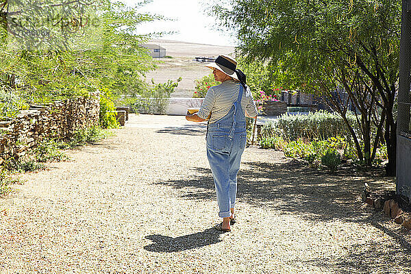 Frau in Overalls geht an sonnigem Tag im Garten spazieren