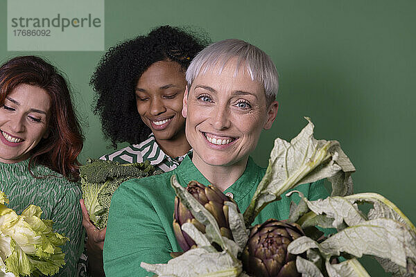 Fröhliche gemischtrassige Freunde mit frischem rohem Gemüse vor grünem Hintergrund