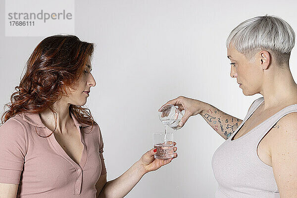 Frau füllt das Glas eines Freundes mit Wasser und steht vor weißem Hintergrund