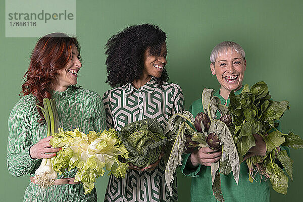 Fröhliche Freunde mit Gemüse vor grünem Hintergrund