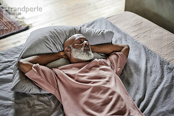 Mann mit Glatze und geschlossenen Augen ruht sich zu Hause im Bett aus
