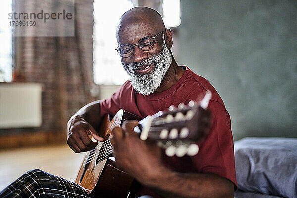 Lächelnder reifer Mann  der zu Hause Gitarre spielt