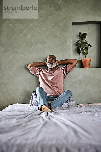 Mann mit Händen hinter dem Kopf entspannt sich zu Hause im Bett