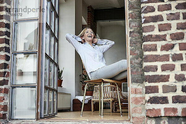 Glückliche Frau sitzt auf einem Stuhl auf der Terrasse