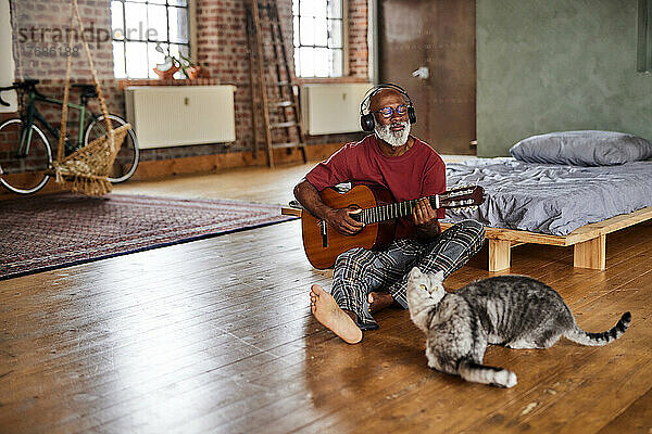 Reifer Mann spielt zu Hause im Schlafzimmer Gitarre mit Katzen