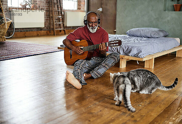 Mann spielt zu Hause vor Katzen Gitarre