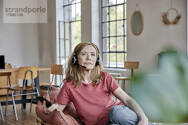 Frau mit Headset sitzt zu Hause im Wohnzimmer