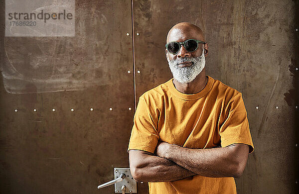 Glatzköpfiger Mann mit Sonnenbrille steht mit verschränkten Armen vor der Tür