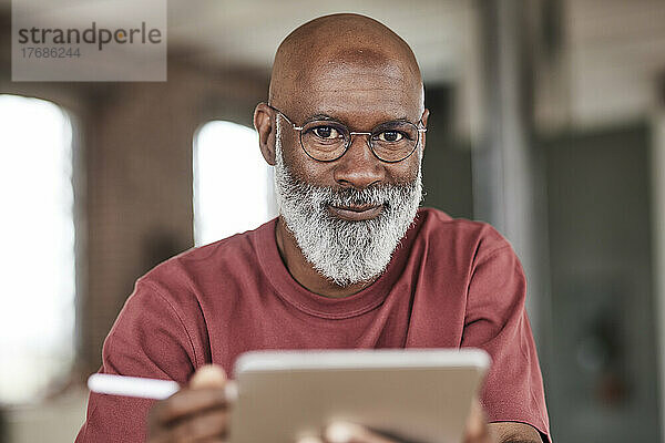 Reifer Mann mit Bart hält Tablet-PC zu Hause
