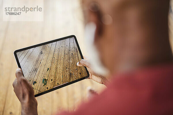 Mann fotografiert Hartholzboden mit Tablet-PC zu Hause