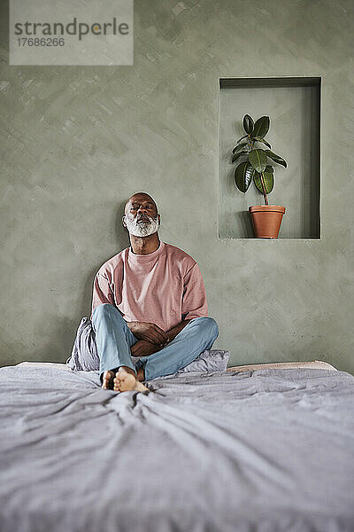 Mann mit weißem Bart sitzt zu Hause im Bett