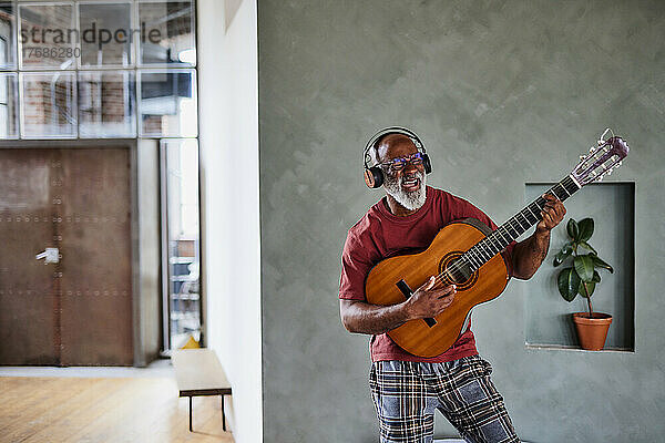 Mann mit Kopfhörern  der zu Hause Gitarre spielt und singt