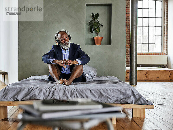 Geschäftsmann  der zu Hause im Bett sitzt und Musik über drahtlose Kopfhörer hört