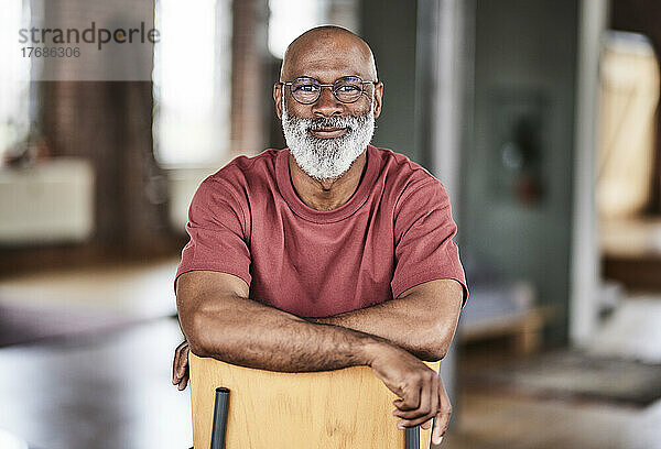 Glatzköpfiger Mann mit Brille auf Stuhl zu Hause