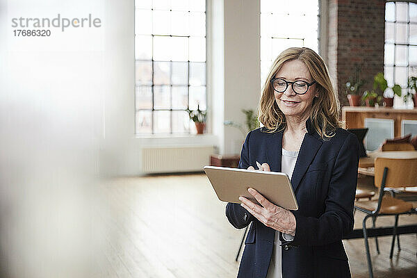 Lächelnde Geschäftsfrau mit Tablet-PC im heimischen Wohnzimmer