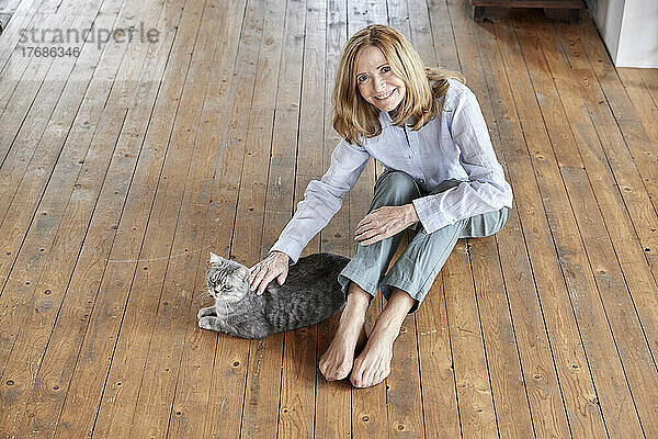Lächelnde Frau mit Katze sitzt zu Hause auf dem Boden