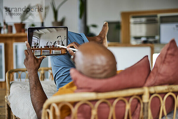 Glatzköpfiger Mann mit digitalisiertem Stift und Tablet-PC  der zu Hause auf dem Sofa liegt