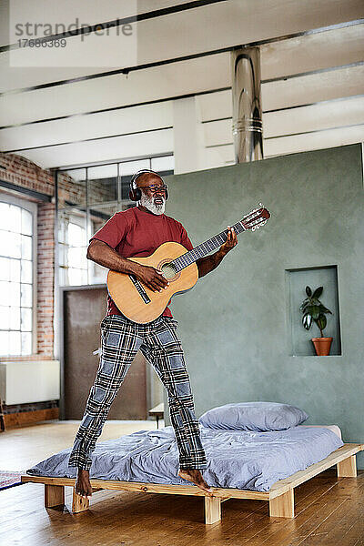 Reifer Mann springt und spielt Gitarre im Schlafzimmer