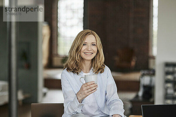 Glückliche Frau mit Kaffeetasse  die zu Hause sitzt