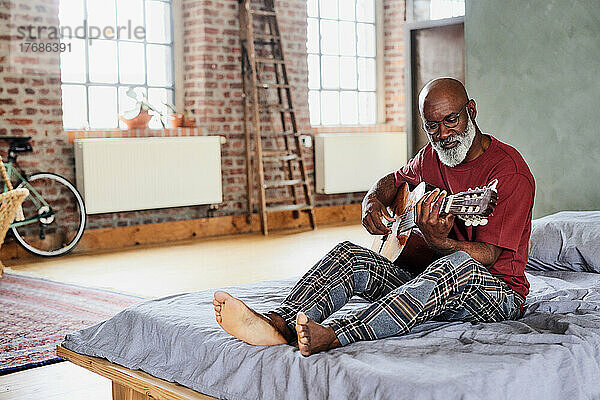Mann mit Brille spielt zu Hause im Bett Gitarre