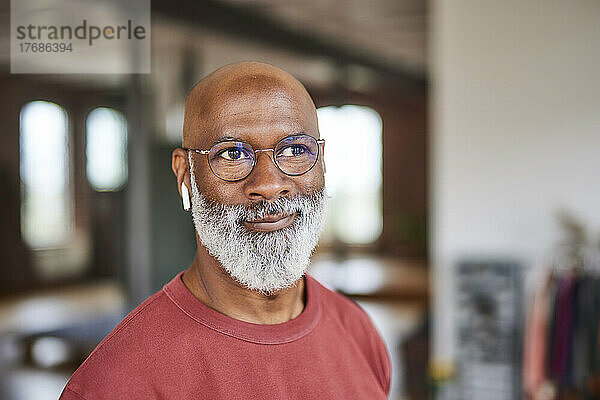 Lächelnder Mann mit Glatze und grauem Bart  der zu Hause eine Brille trägt