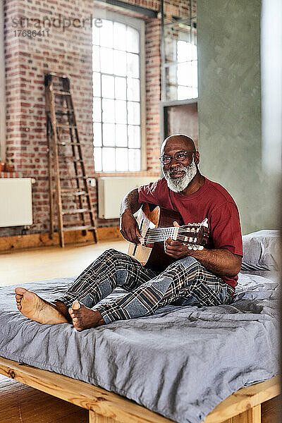 Reifer Mann mit Brille spielt zu Hause im Bett Gitarre