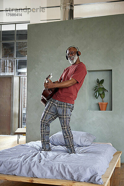 Reifer Mann mit Kopfhörern  der zu Hause im Bett Gitarre spielt