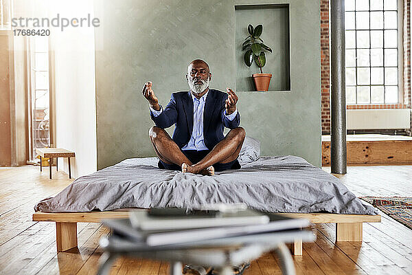 Reifer Geschäftsmann meditiert auf dem Bett im Schlafzimmer zu Hause