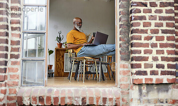 Bald man using laptop sitting on chair at home